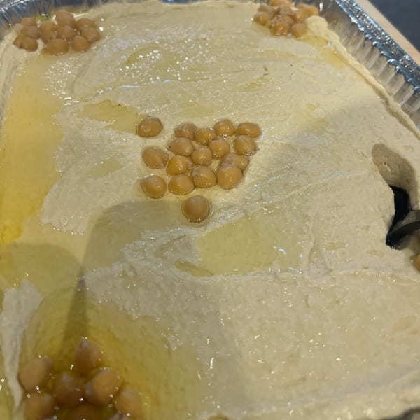 Creamy hummus with olive oil and chickpeas in a silver foil tray, ready to be served.