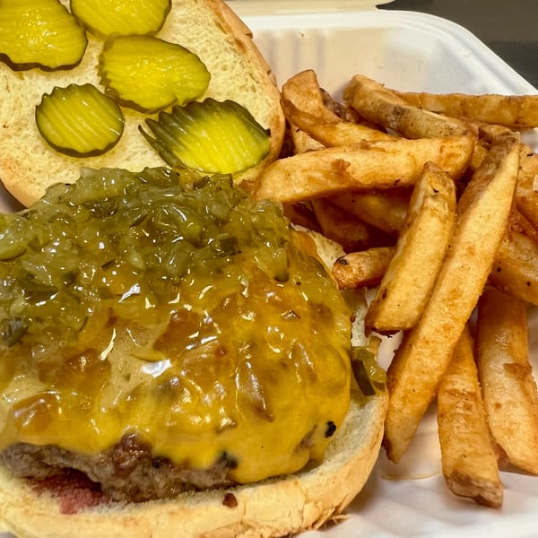 A Burger Shack cheeseburger with relish and pickles, served with a side of golden fries.