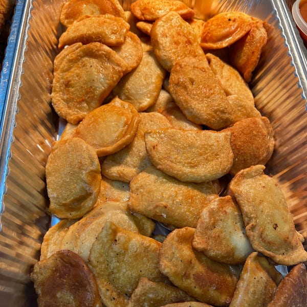 A close-up of golden-brown, fried empanadas or dumplings in a metallic serving tray.