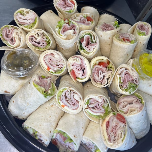 A platter of various deli meat and cheese wraps with lettuce and tomato, served with dipping sauces.