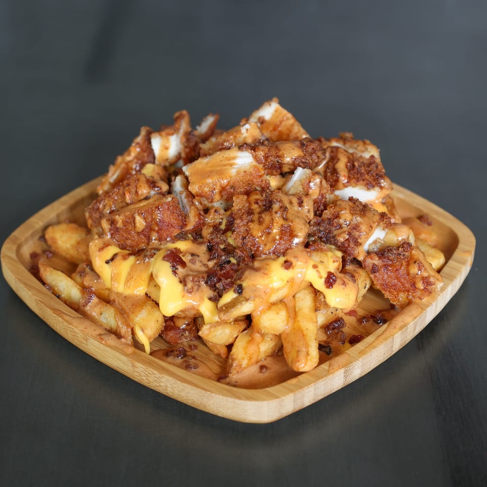 The Burger Shack's loaded fries with crispy chicken, cheese sauce, and bacon bits on a wooden platter.