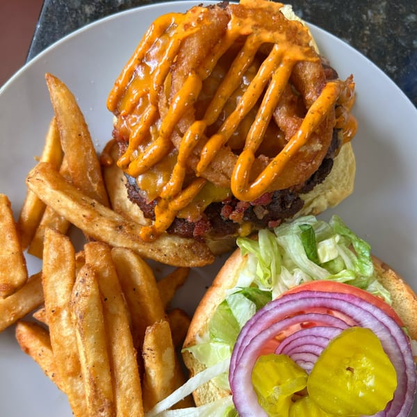 A Burger Shack burger with onion rings and special sauce, served with a side of fries.