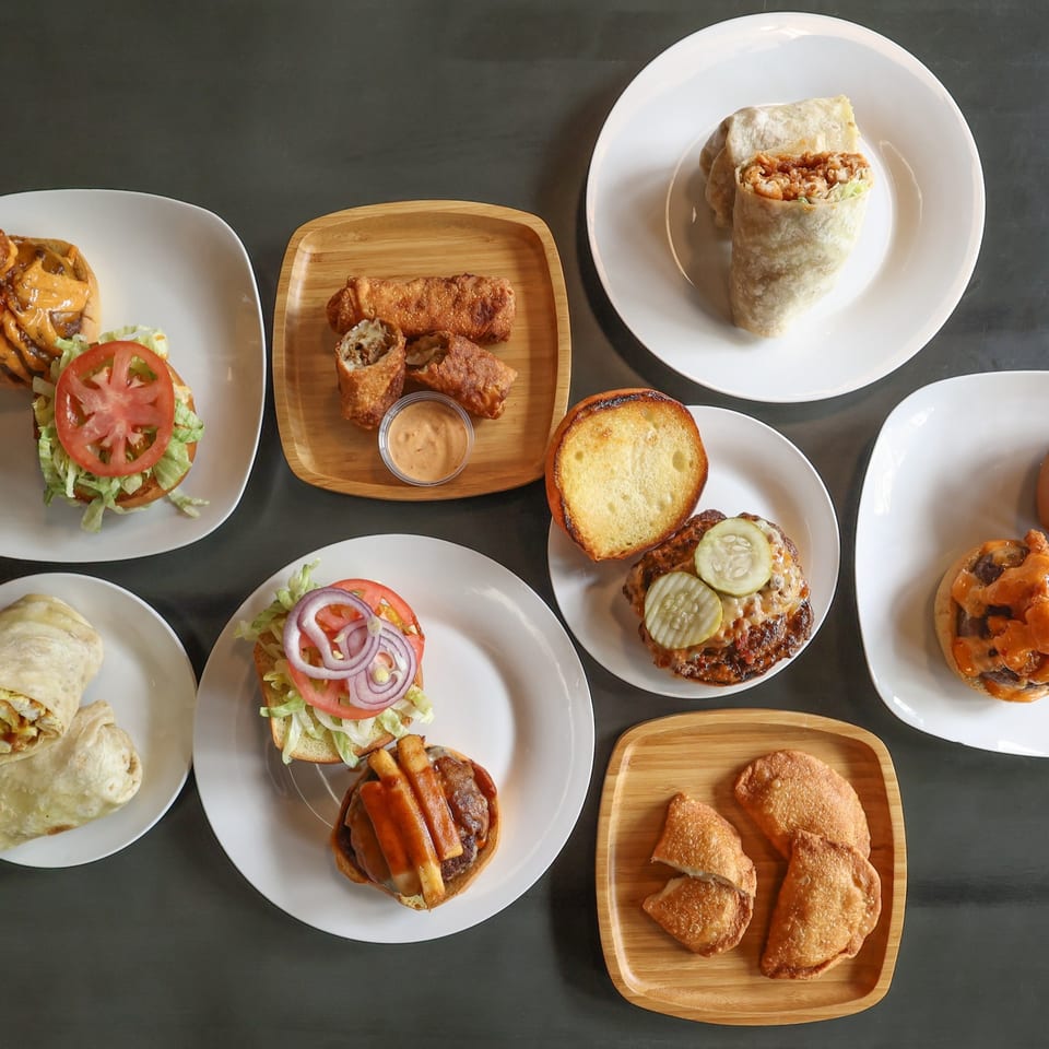 An overhead shot of various Burger Shack menu items, including burgers, wraps, egg rolls, and empanadas.