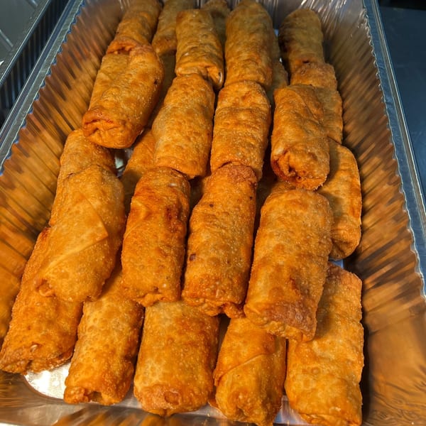 Crispy golden-brown egg rolls, freshly fried and arranged in a silver foil tray.