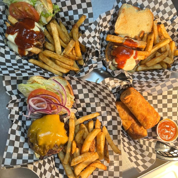 Four baskets of The Burger Shack's burgers and fries, with two egg rolls and dipping sauce.
