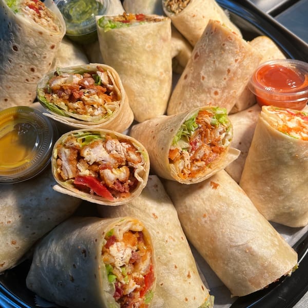 A platter of The Burger Shack's chicken wraps, some cut open to show filling, with dipping sauces.