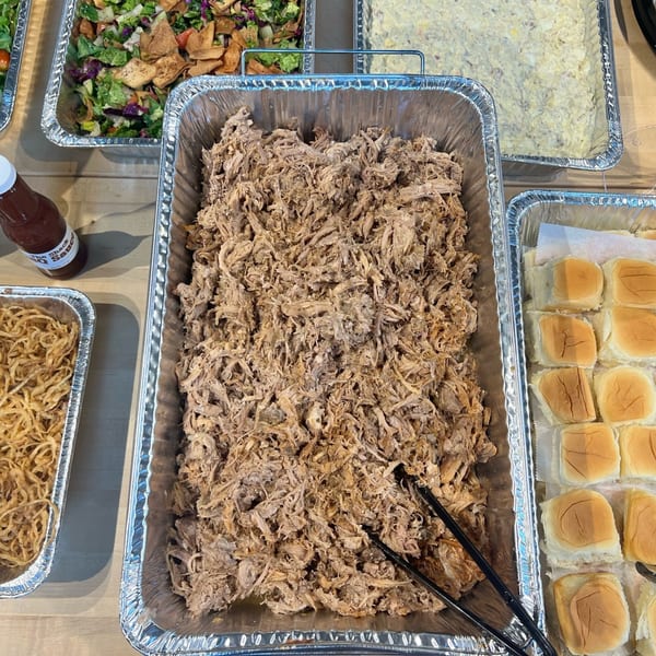 Catering spread with pulled pork, slider buns, crispy onions, salad, and potato salad.