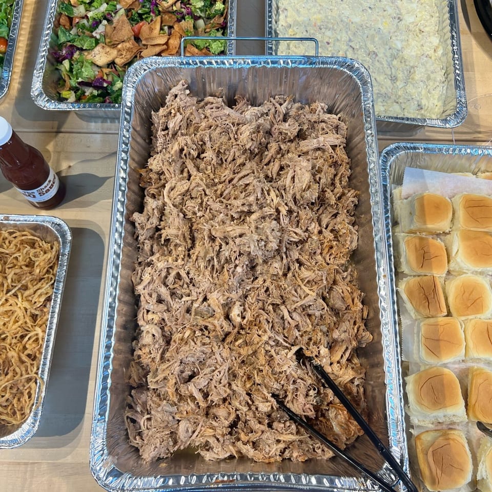 Catering spread with pulled pork, slider buns, crispy onions, salad, and potato salad.