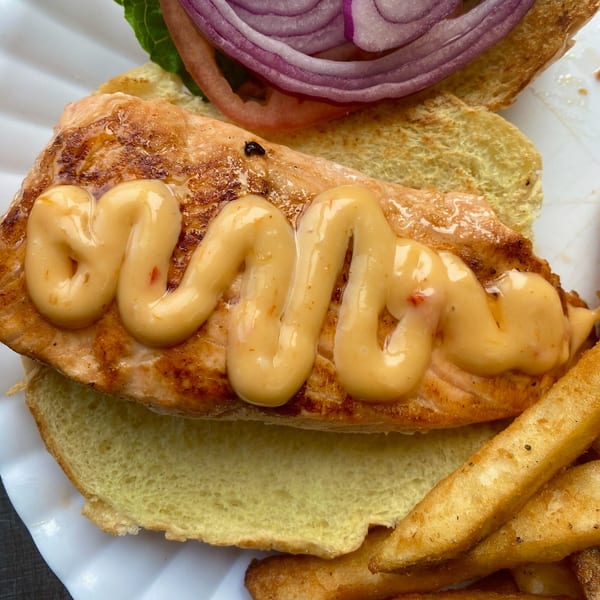 A salmon burger with sauce, red onion, lettuce, and fries on a white plate.