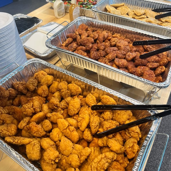 Three aluminum trays of The Burger Shack's fried chicken bites, with plates and cutlery nearby.