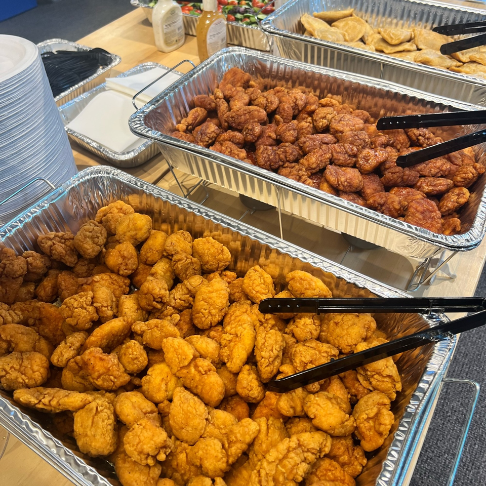 Three aluminum trays of The Burger Shack's fried chicken bites, with plates and cutlery nearby.