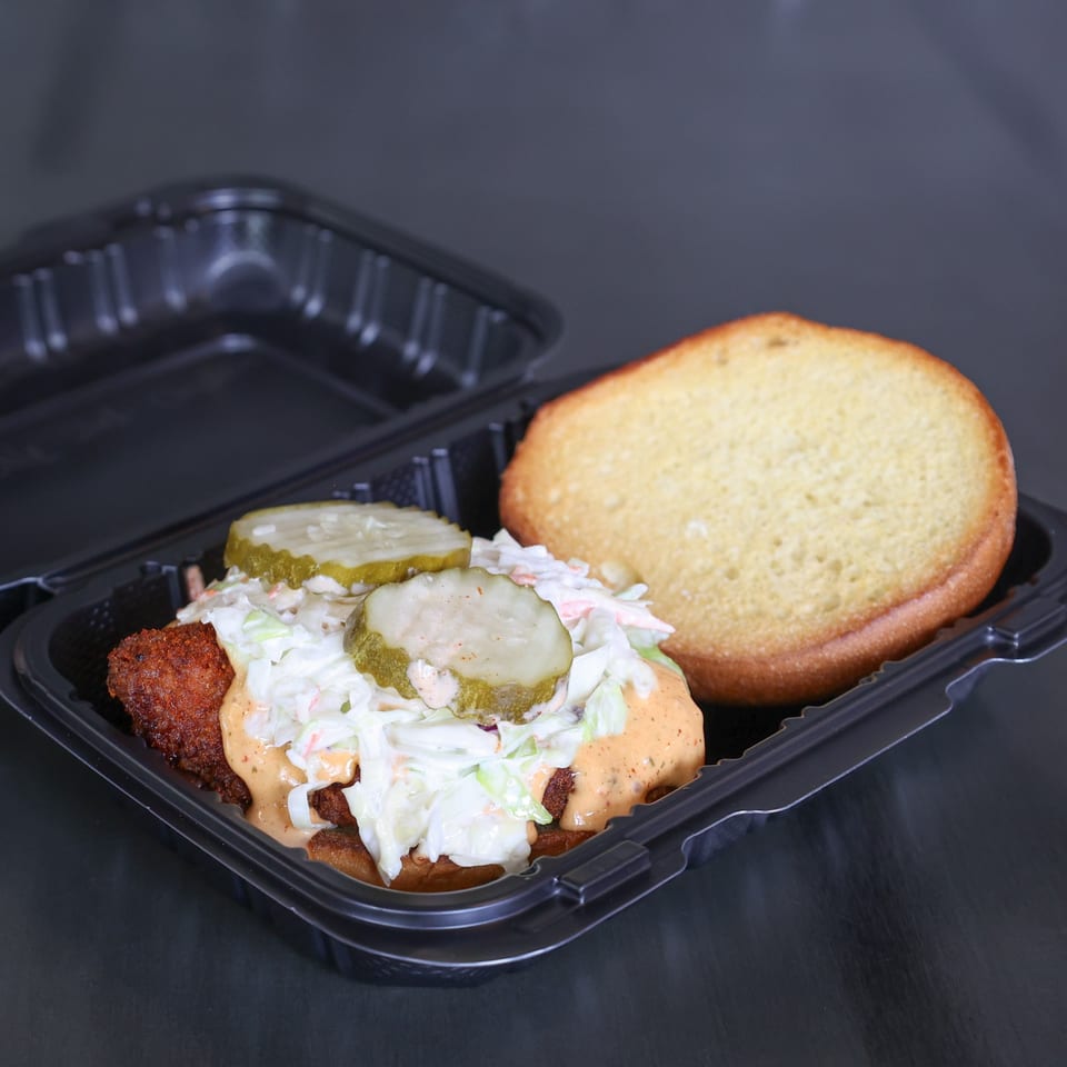 The Burger Shack's fried chicken sandwich with coleslaw, pickles, and sauce in a takeout container.