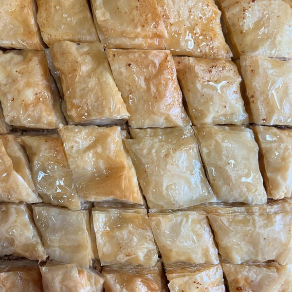 Close-up of golden-brown baklava squares, glistening with sweet syrup and sprinkled with nuts.