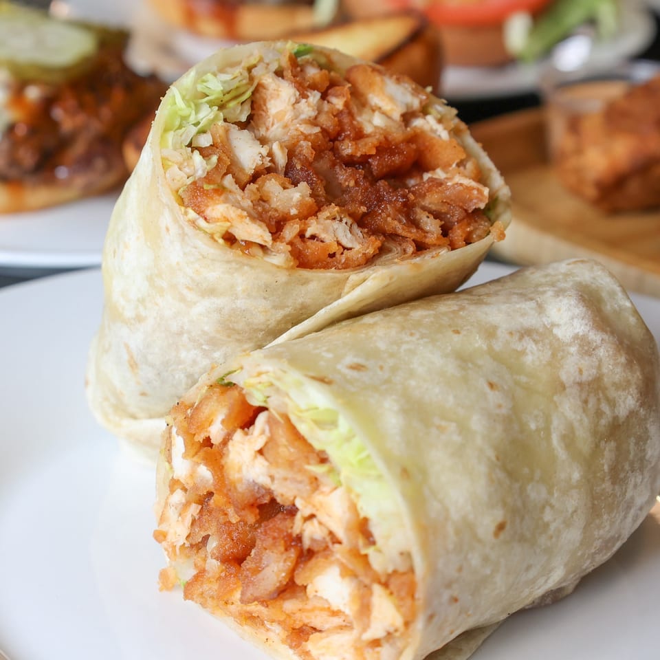 Two halves of a crispy chicken and lettuce wrap on a white plate at The Burger Shack.