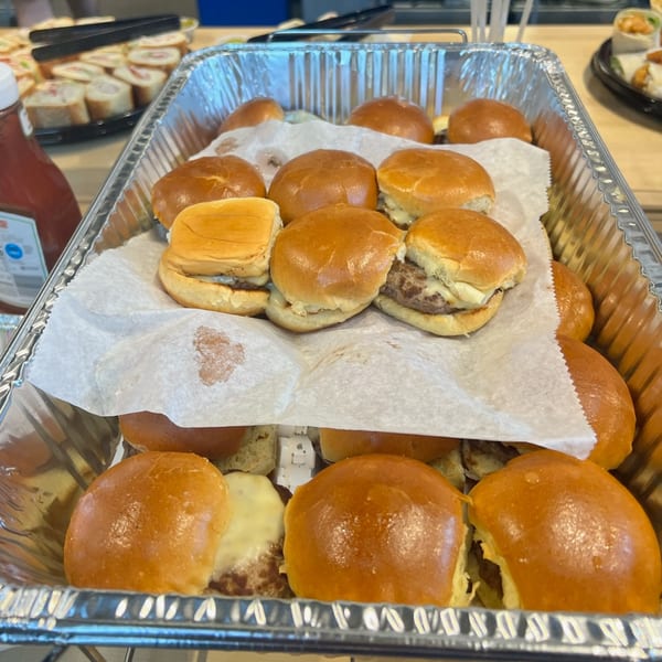 A catering tray filled with numerous mini cheeseburger sliders on soft buns, ready to be served.