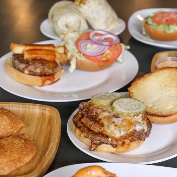 A table laden with various Burger Shack burgers, including one with fries and another with pickles.