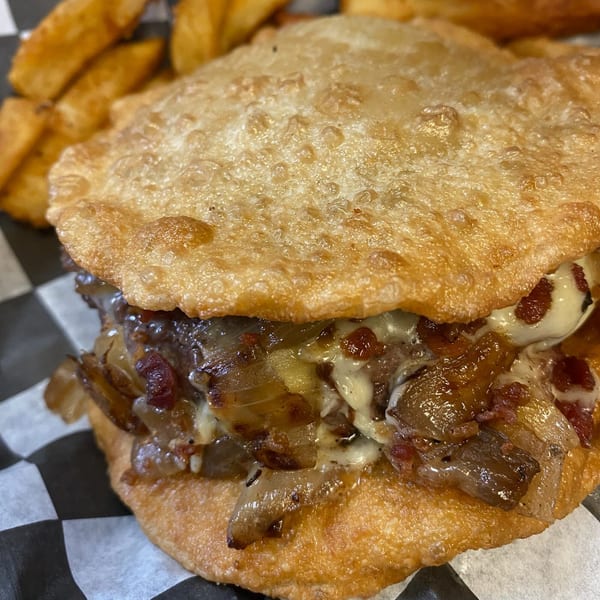 Close-up of a Burger Shack burger with caramelized onions and melted cheese on fried dough.