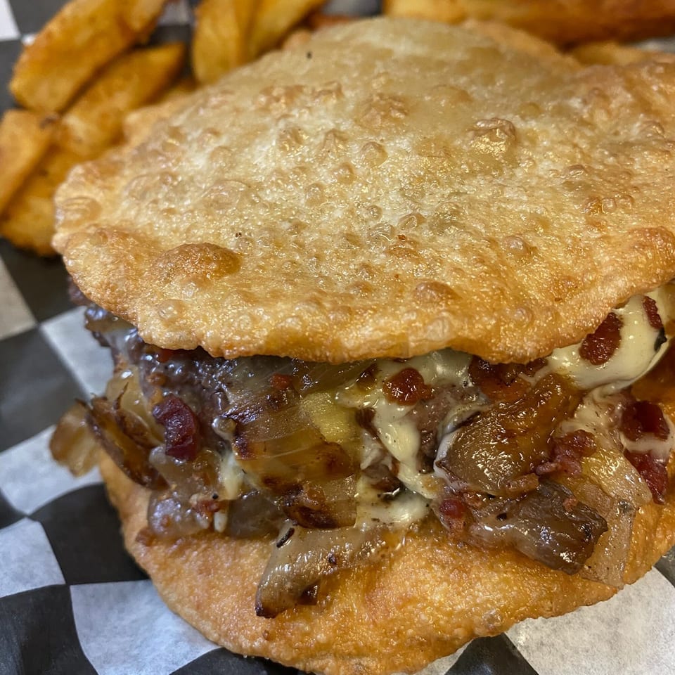 Close-up of a Burger Shack burger with caramelized onions and melted cheese on fried dough.